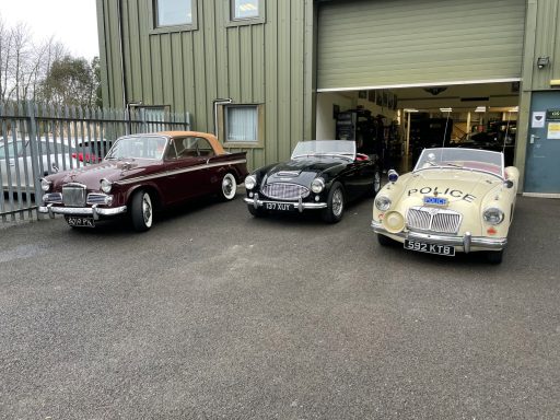 Classic British Motoring Three classic cars parked outside Chichester Classics Ltd, showcasing vintage styles and colours.