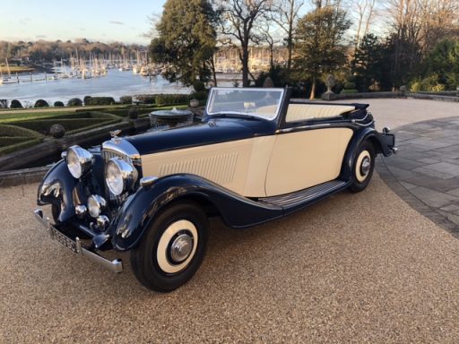Pre war Derby Bentley Classic convertible car in navy blue and cream parked by a scenic waterfront.