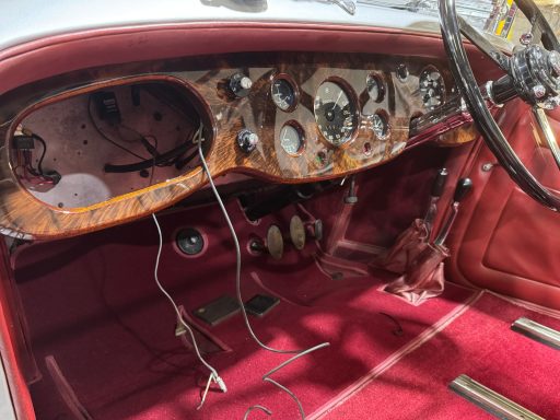 Burr Walnut veneere and lacquered Classic car interior featuring wooden dashboard, vintage gauges, and red upholstery.